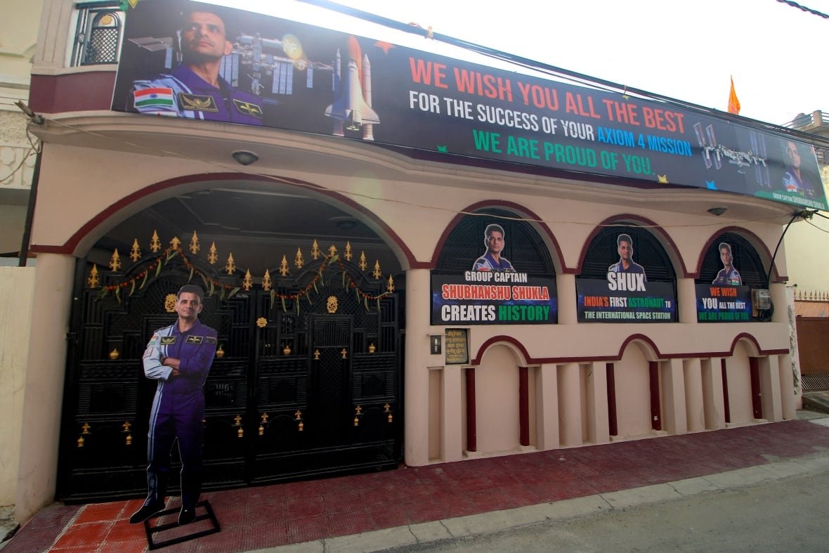 2218787559 A full-body cutout and several images of the same man are displayed outside a building alongside images of a space shuttle and a space station. The text reads, "WE WISH YOU ALL THE BEST/FOR THE SUCCESS OF YOUR AXIOM 4 MISSION/WE ARE PROUD OF YOU."