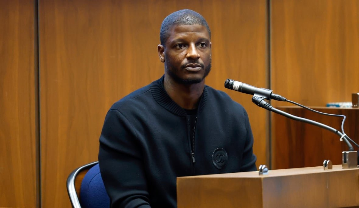 a-ap-rocky-shooting-trial-1 A man sits at a wooden podium with a microphone pointed at him.