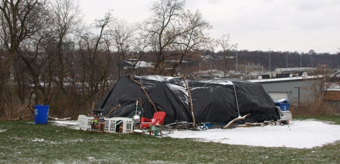bayfront-encampment A tent covered in a black tarp surrounded by a plastic chair and a fence.