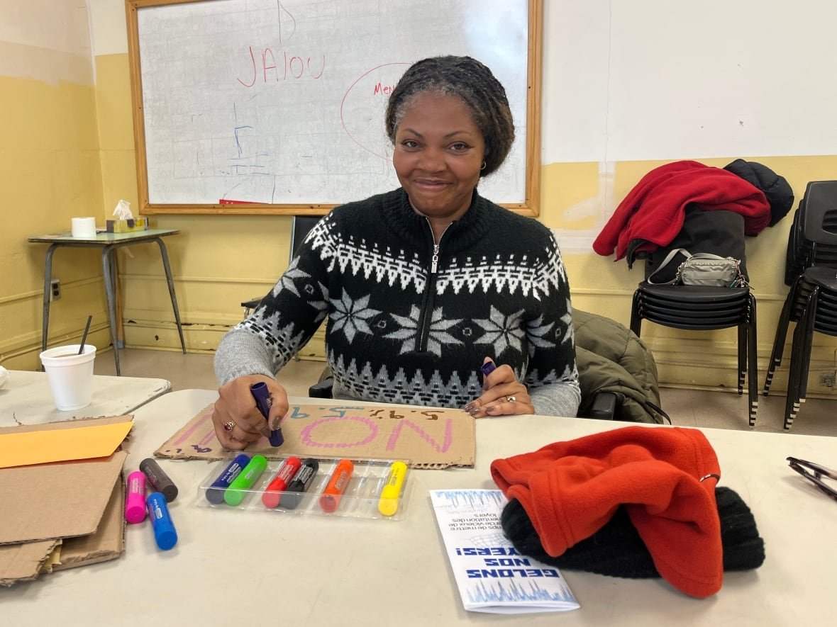 belynda-joseph A Black woman writes on a cardboard sign.