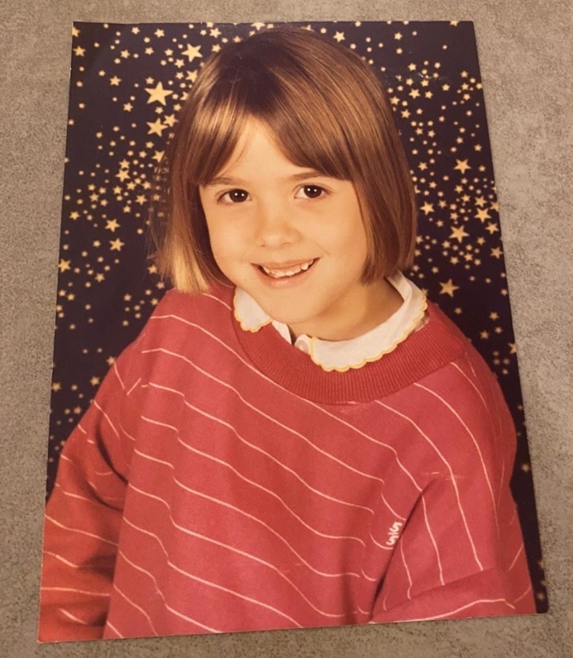 caroline-darian-childhood-photo A studio portrait of a young girl with brown hair wearing a red-and-white striped sweater.