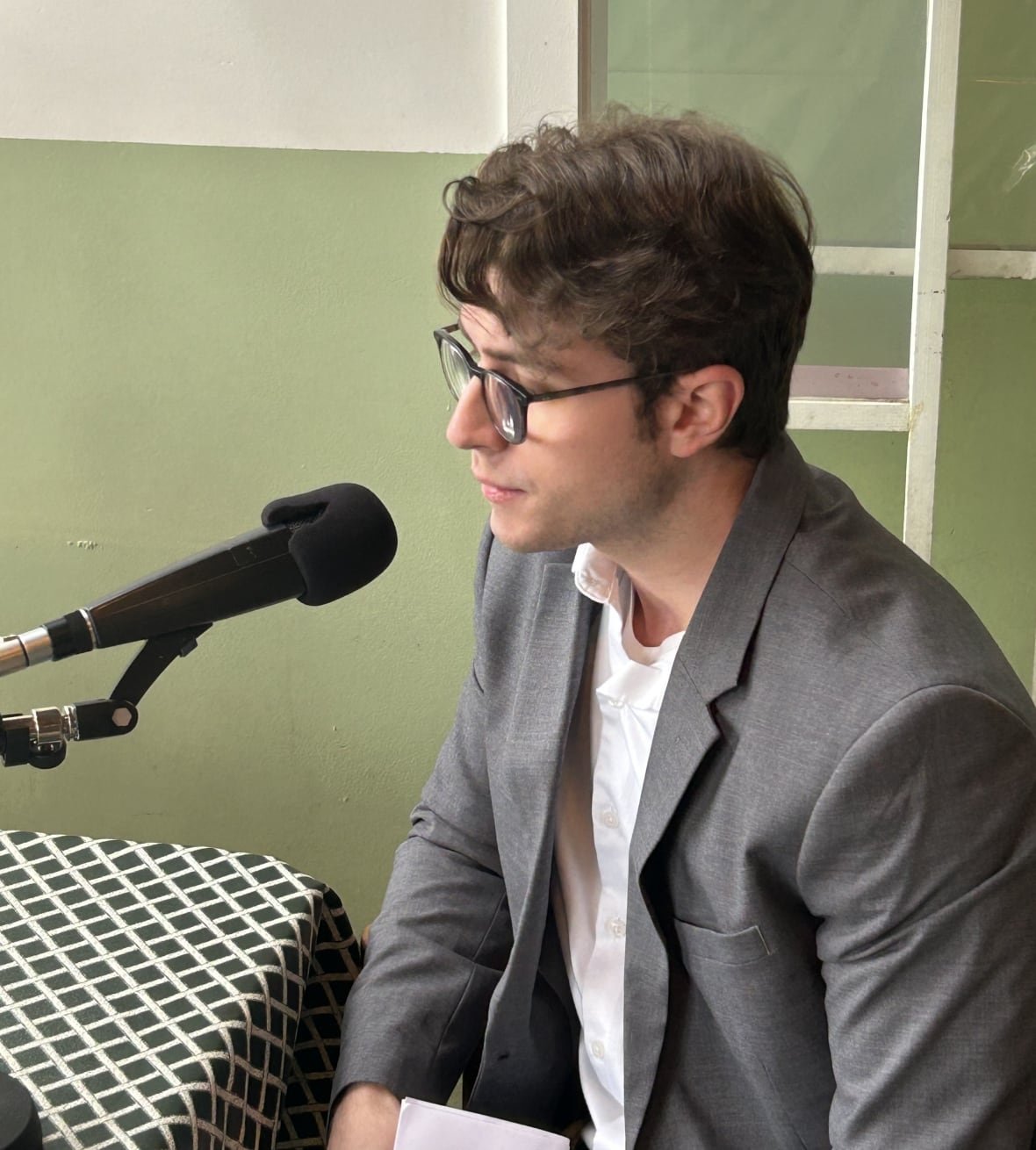 connor-kuznik A young man with glasses and a grey blazer speaks into a microphone at a diner