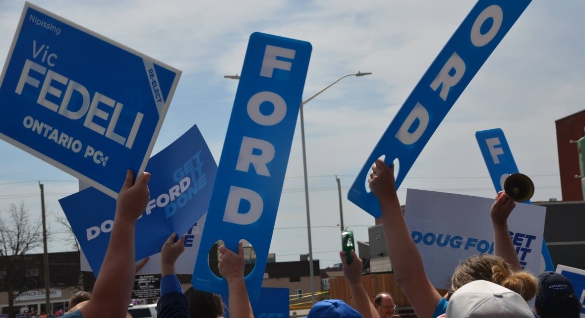 doug-ford-vic-fedeli-supporters-2022 A crowd of people holding up blue election signs reading 'Ford' and 'Vic Fedeli'