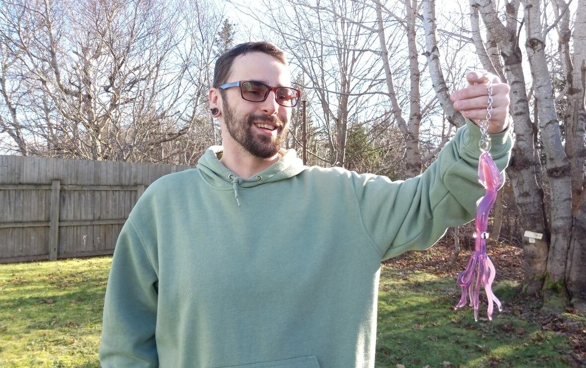 josh-moores-1 Man in green hoodie holding in a glass squid ornament in backyard.