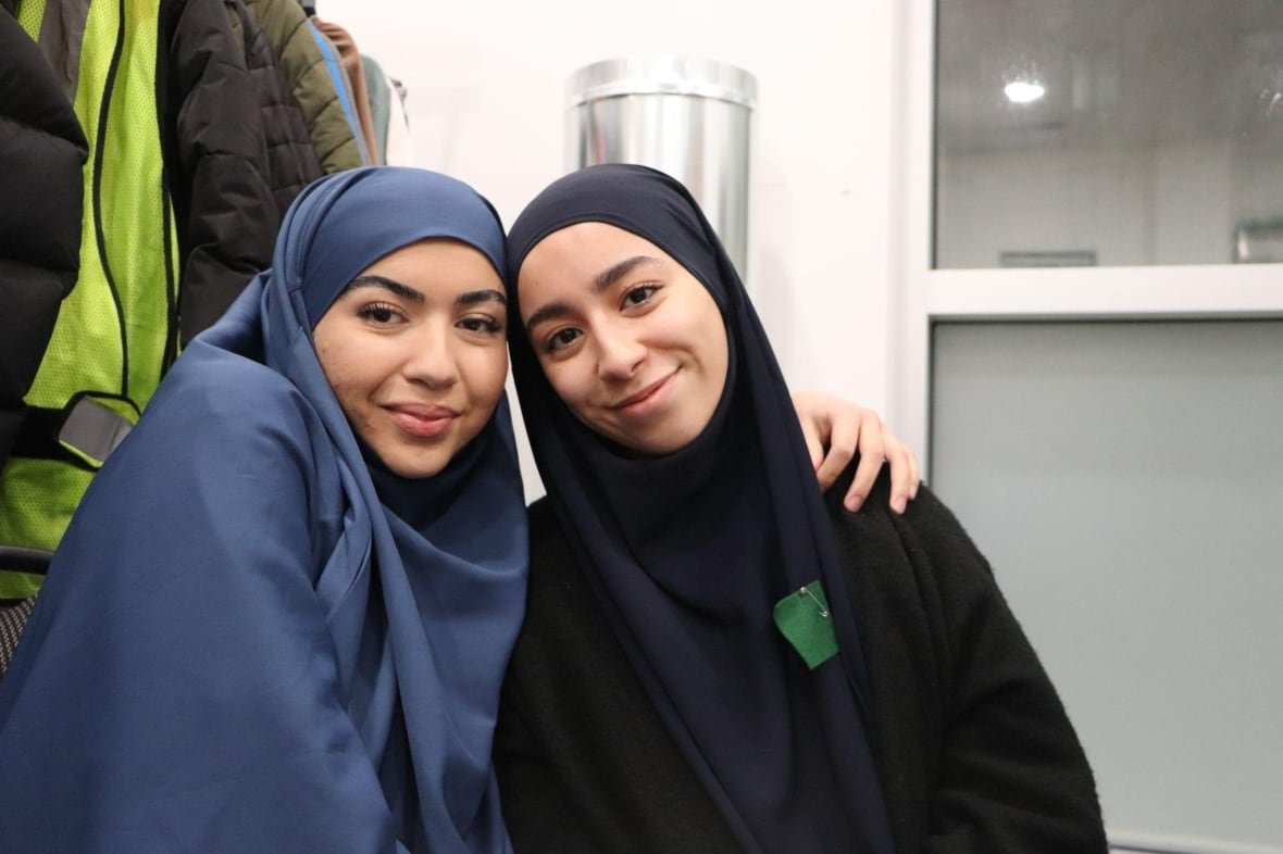 nesrine-adda-and-sakina-ouchane Two women wearing hijabs smile, wraping their arms around eachother