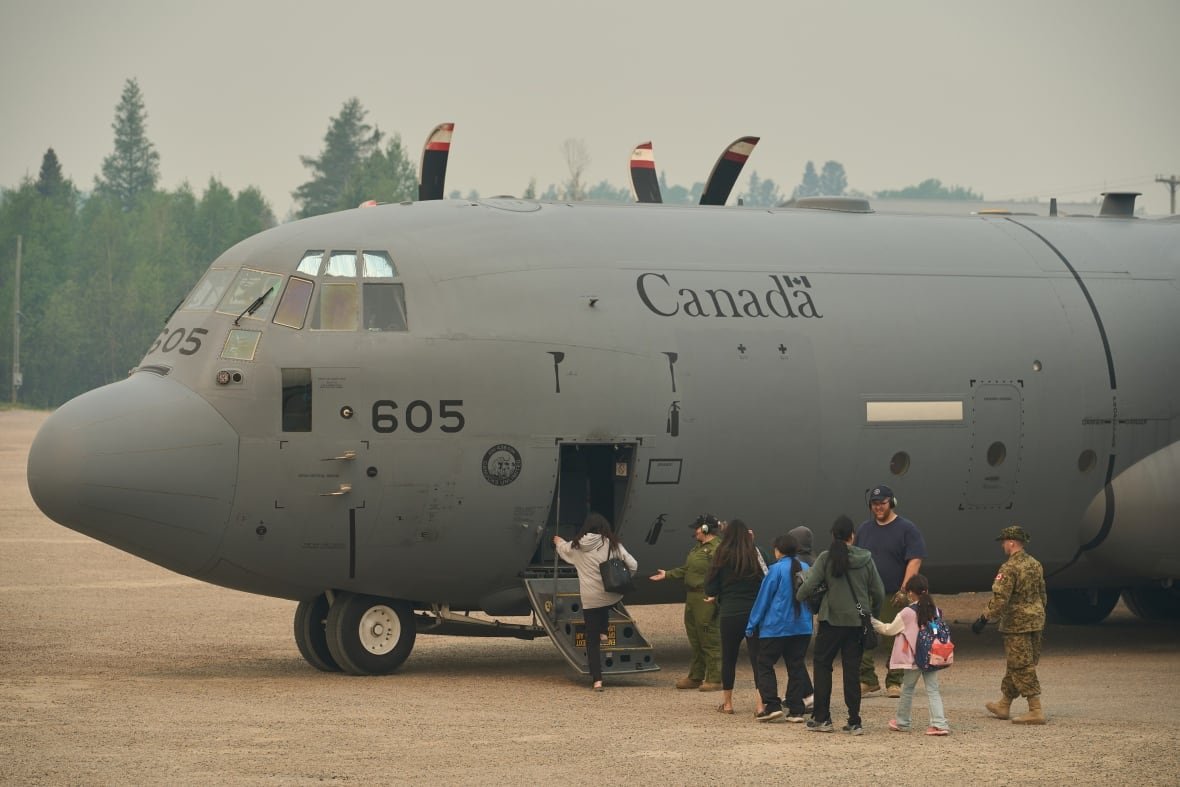 prairies-wildfires-20250603 People board a large military aircraft as smoke fills the air around them.