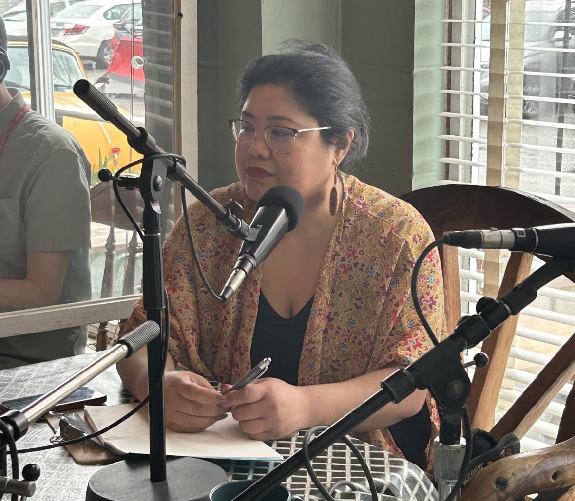 sammie-jo-rumbaua A woman with glasses and dark hair sits behind a microphone at a diner table