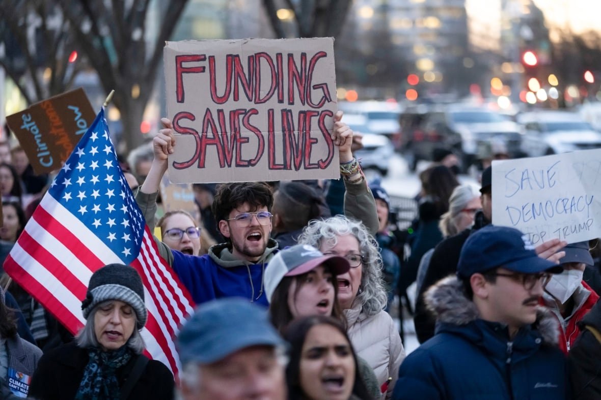 trump-federal-aid A protester holds up a sign that reads, 'Funding saves lives,' during a demonstration.