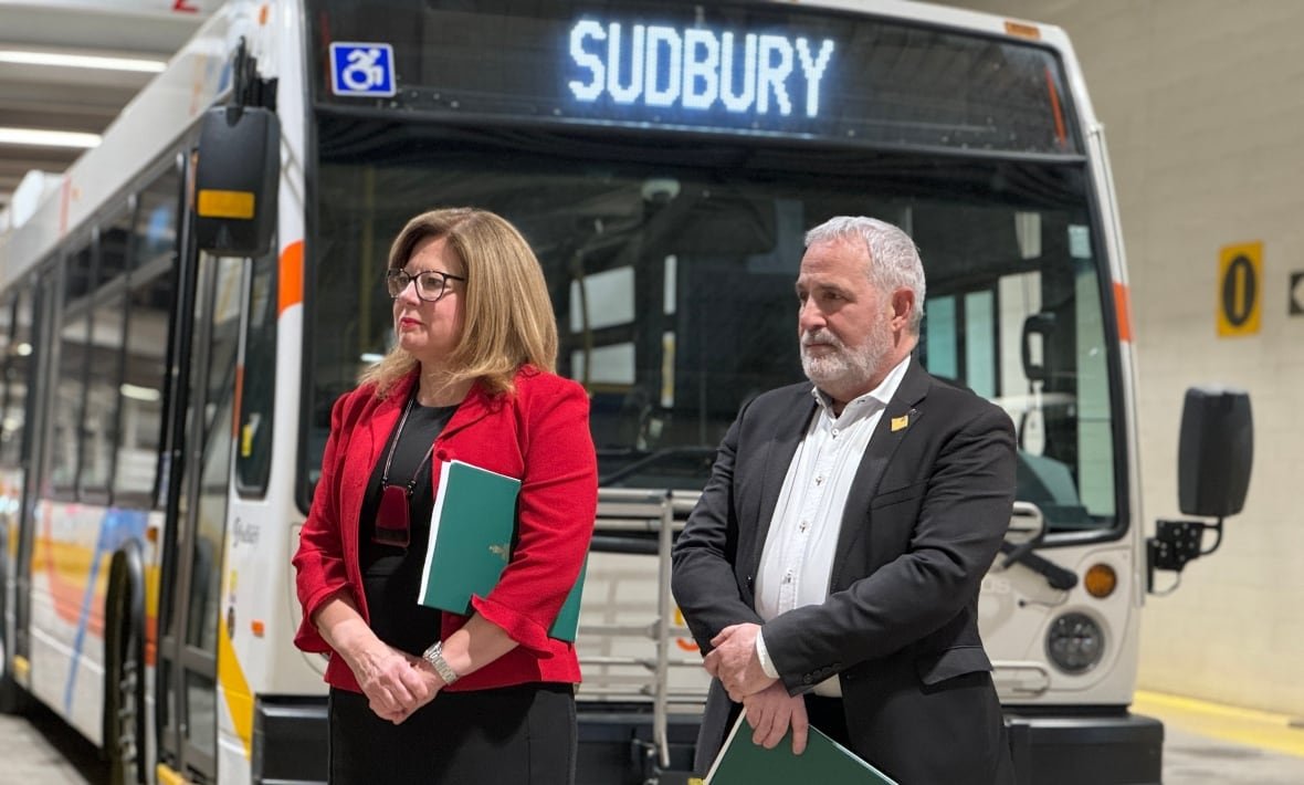 viviane-lapointe-and-marc-serre A woman in red and man in a suit standing in front of a parked bus.
