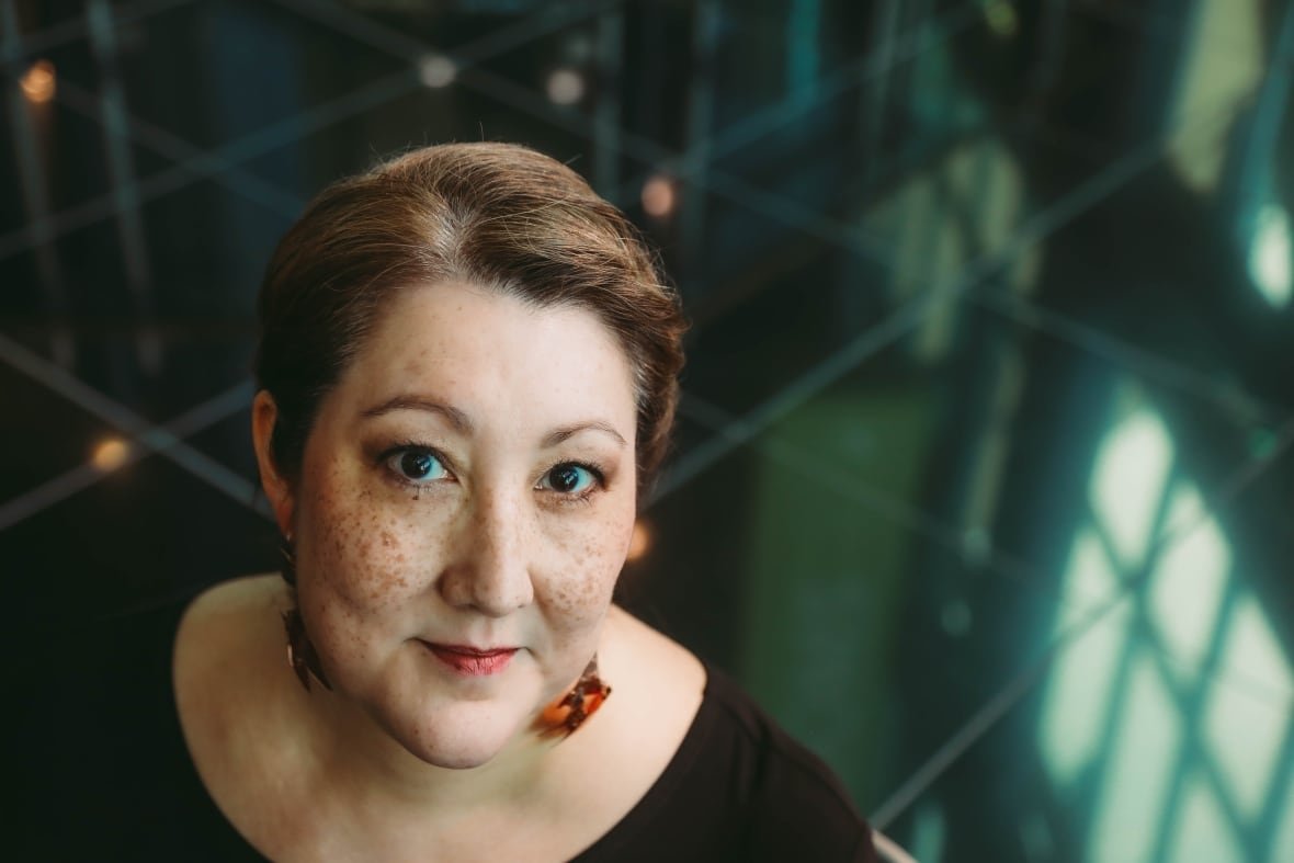Deatha wears a black top while looking upwards from a green tiled floor.