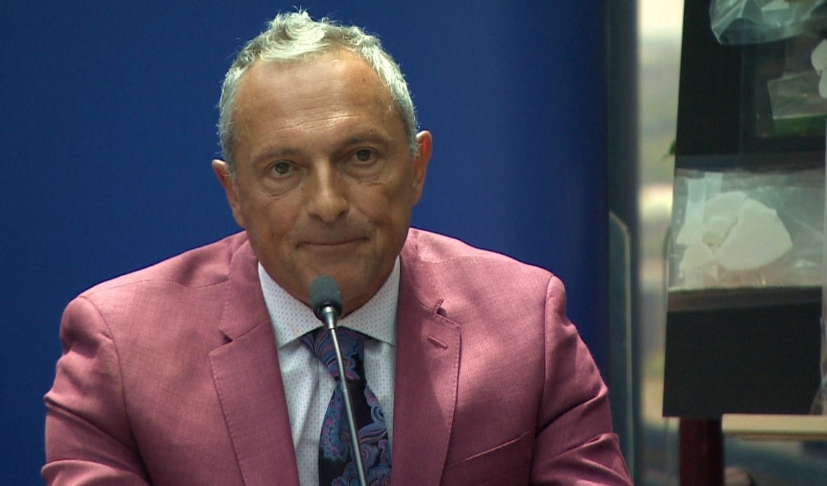 Man in red blazer sits in front of microphone.