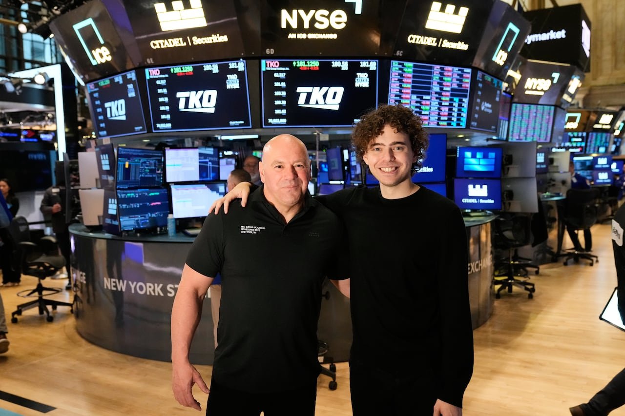 two men with their arms around each other pose for a photo on the floor of the New York Stock Exchange