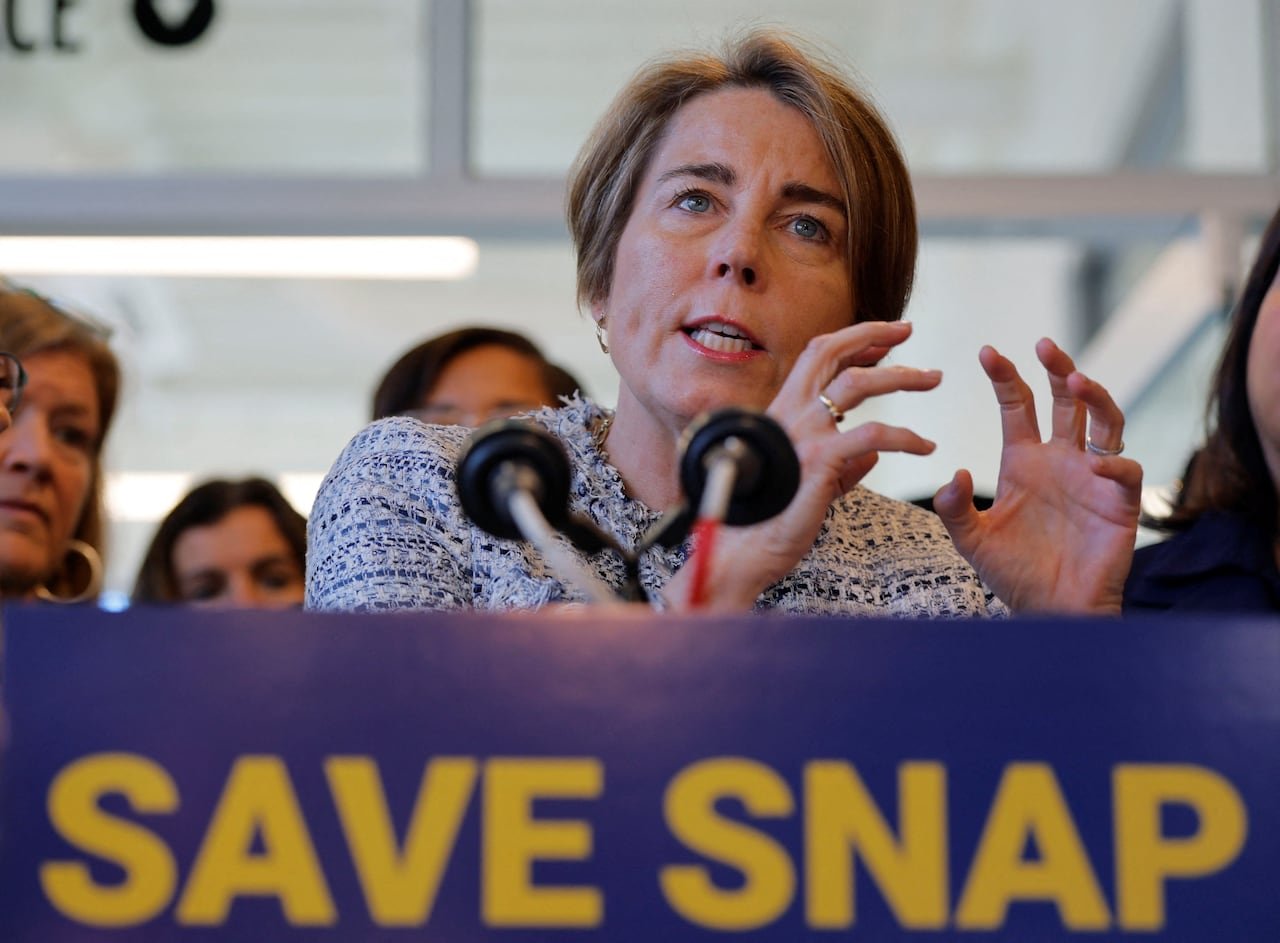 A woman with hair that goes to her ears gestures in a closeup shot while speaking at a podium that has a placard on front that says, "Save Snap."
