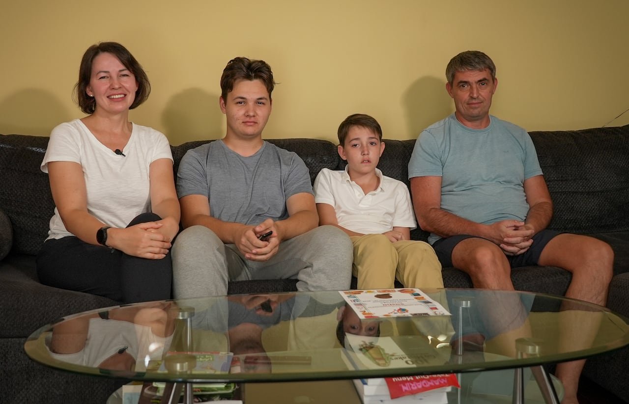A family of four, including a mom, dad and two sons, sit on a couch in a living room.