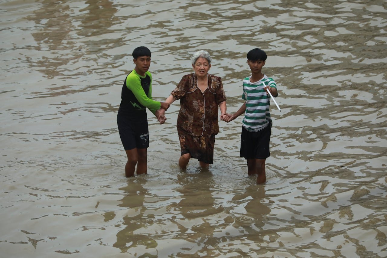 default-468 An elderly woman is assisted through flood waters by two boys.