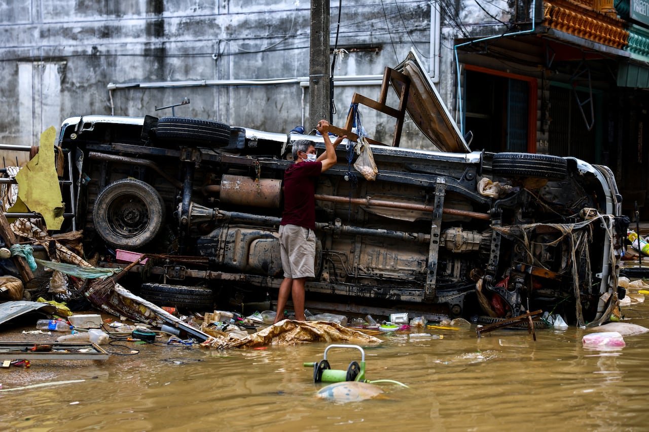 default-469 A man stands next to a damaged car in a flooded area.